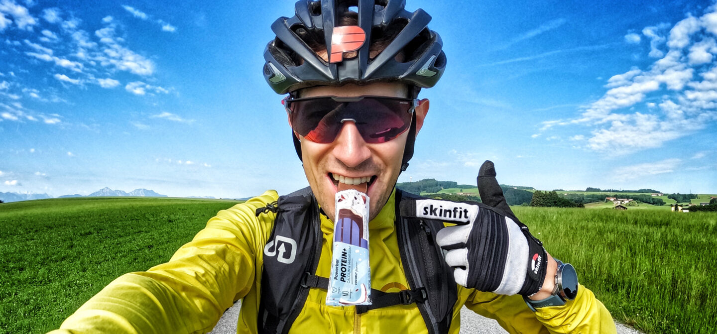 A bike rider, pointing to a PowerBar that they are enjoying.